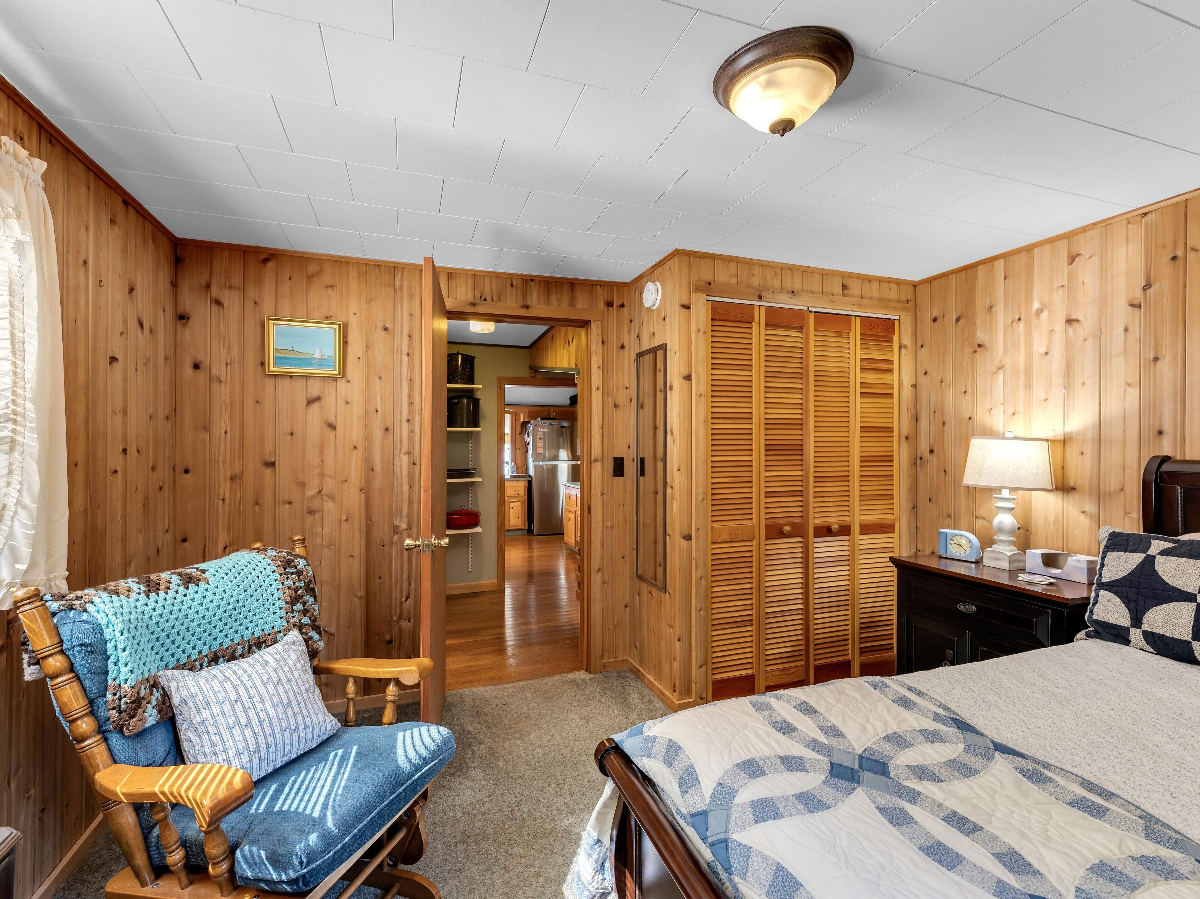 Een kamer met houten lambrisering, een bed, een stoel, een nachtkastje en een garderobe.