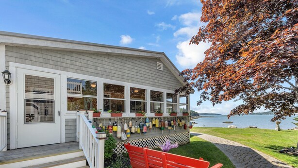 A waterfront property with a porch displaying various decorative items, a red bench, and a view of the water.