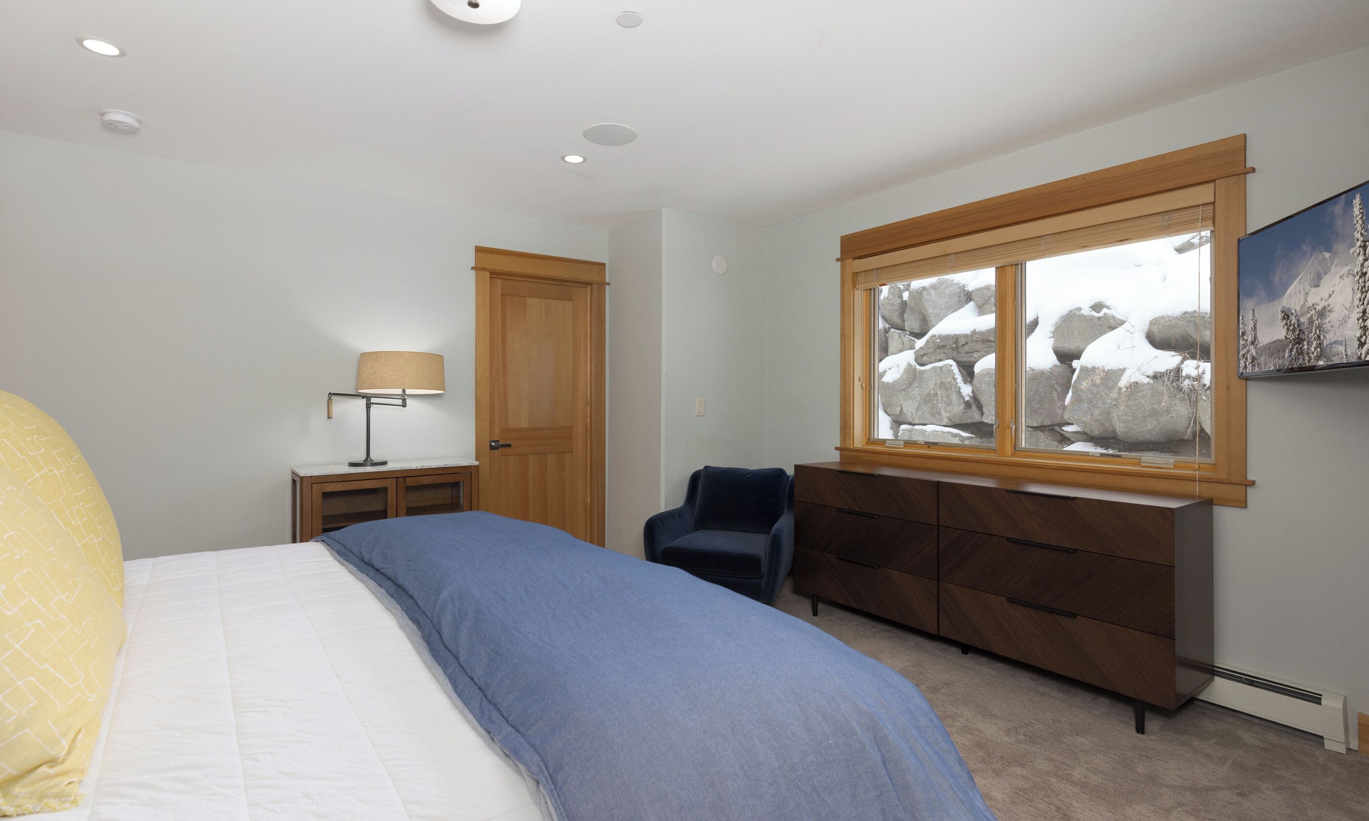 Unwind in your serene bedroom featuring warm wood accents, plush bedding, and peaceful views of snow-dusted boulders through the picture window.