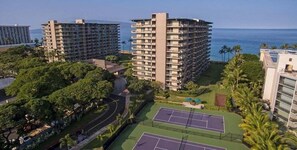 A high-rise hotel with multiple balconies, a tennis court, and a view of the ocean.