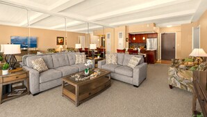 Ein Wohnzimmer mit zwei grauen Sofas, einem Couchtisch und einer sichtbaren Küche im Hintergrund.