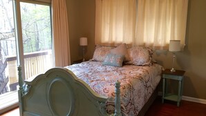Une chambre avec un grand lit, une table de chevet, deux lampes et une vue sur les arbres par la fenêtre.