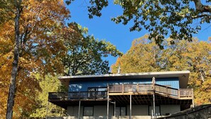 Un bâtiment moderne à deux étages, doté d’un toit plat, d’un balcon au deuxième étage et d’un mur de soutènement en pierre en premier plan.