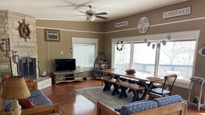 Un salon chaleureux avec une cheminée en pierre, des meubles en bois, un téléviseur et un coin repas comprenant une table et des bancs.