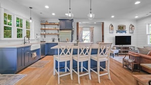 A modern kitchen with blue cabinets, a dining area with white chairs, and a living room with a TV and seating.