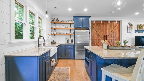 A modern kitchen with blue cabinets, a stainless steel refrigerator, and a wooden barn door.