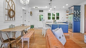 A modern kitchen with white cabinetry, a blue accent wall, and a dining area with a wooden table and bench.