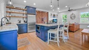 A modern kitchen with blue cabinets, stainless steel appliances, and wooden flooring.