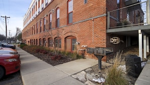 A red brick building with a row of windows and a small balcony. There are cars parked on the street in front. - Cozy Loft U of M Dinkytown (Minneapolis)