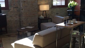A cozy room with a brick wall, a sofa, a small table with a lamp, and a potted plant. - Cozy Loft U of M Dinkytown (Minneapolis)
