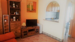 A living room with a television on a wooden stand, a bookshelf, a painting, and a window overlooking a balcony. - Beautiful house in urb. international (Gran Alacant)