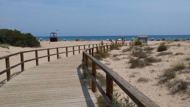 A wooden boardwalk leading to a beach with people sunbathing and umbrellas. - Beautiful house in urb. international (Gran Alacant)