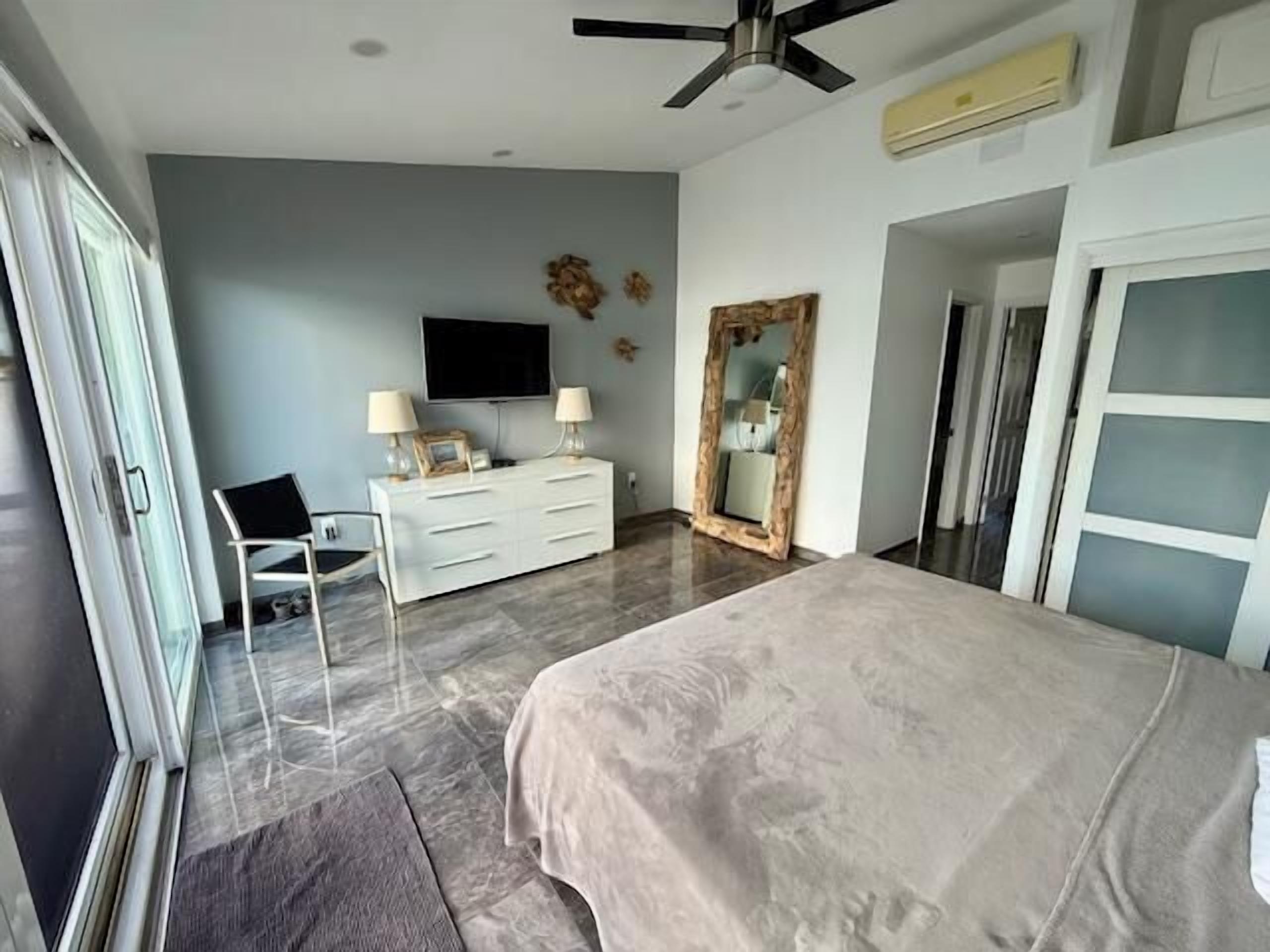 A bedroom with a bed, a dresser, a TV, and a mirror.