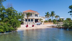 A two-story beachfront property with a clear view of the ocean, a sandy beach, and several palm trees. - Private Island Beachfront Villa 1 Min From Village (Placencia)