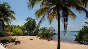 A beach with palm trees, a thatched-roof hut, and a calm sea with boats. - Private Island Beachfront Villa 1 Min From Village (Placencia)