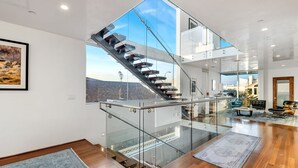 A modern interior with a glass staircase leading to an upper level, a wooden floor, and a view of the outside.