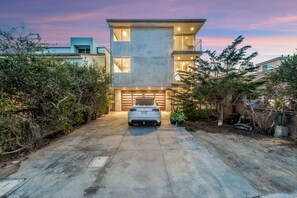 Une maison moderne à deux étages avec un garage, entourée d’une végétation luxuriante et sous un ciel dégagé.