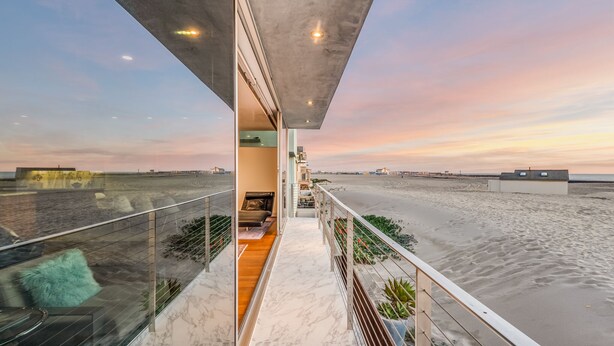 A modern balcony with a view of the beach, a concrete structure overhead, and a glass railing.