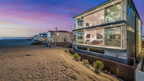 A modern beachfront property with a spacious balcony, large windows, and a view of the beach.