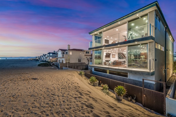 Une propriété moderne située en bord de mer, dotée d’un balcon spacieux, de grandes fenêtres et offrant une vue sur la plage.