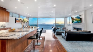 A modern kitchen with a marble countertop, wooden cabinets, and a view of the sea.