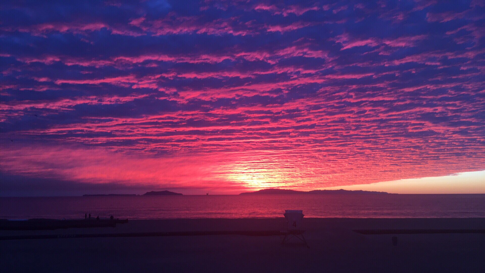 A beach with a sunset, a chair, and a distant shoreline.