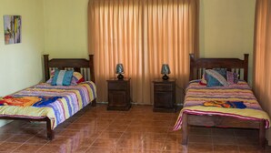 A room with two wooden beds, each with a headboard, a bedside table, and a lamp. The room has a tiled floor and a window with curtains. - Butterfly Cabin - Ocean View-  San Ramon and Esparza (San Ramon)