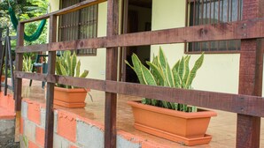 A wooden railing with potted plants, a concrete wall, and a yellow building with windows. - Butterfly Cabin - Ocean View-  San Ramon and Esparza (San Ramon)