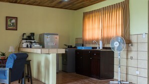 A kitchen with a refrigerator, stove, and a fan. There is a chair and a table with a lamp. - Butterfly Cabin - Ocean View-  San Ramon and Esparza (San Ramon)