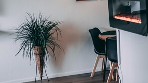 Un comedor con una mesa redonda, sillas negras, una planta en maceta y un televisor montado en la pared.