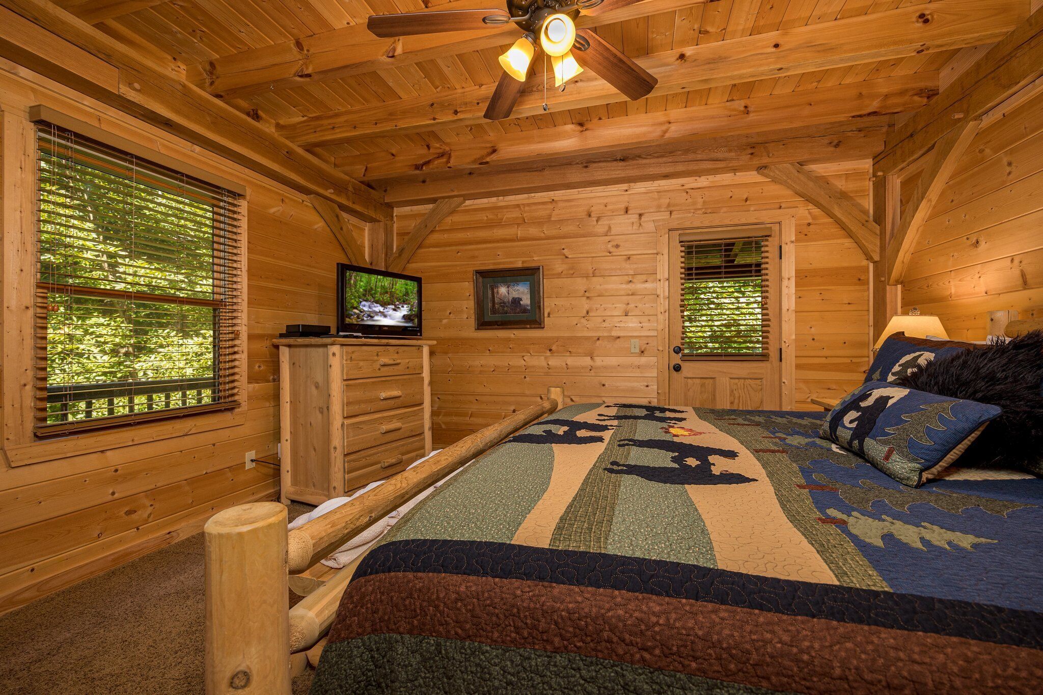 A log cabin bedroom with a bed, dresser, television, and windows.