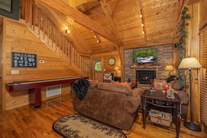 Cozy cabin interior with a fireplace, wooden staircase, and comfortable seating area.