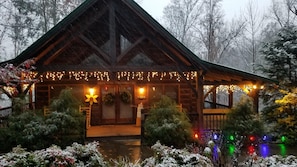 Cozy cabin surrounded by a serene snowy landscape, featuring a charming porch and a peaceful garden area.