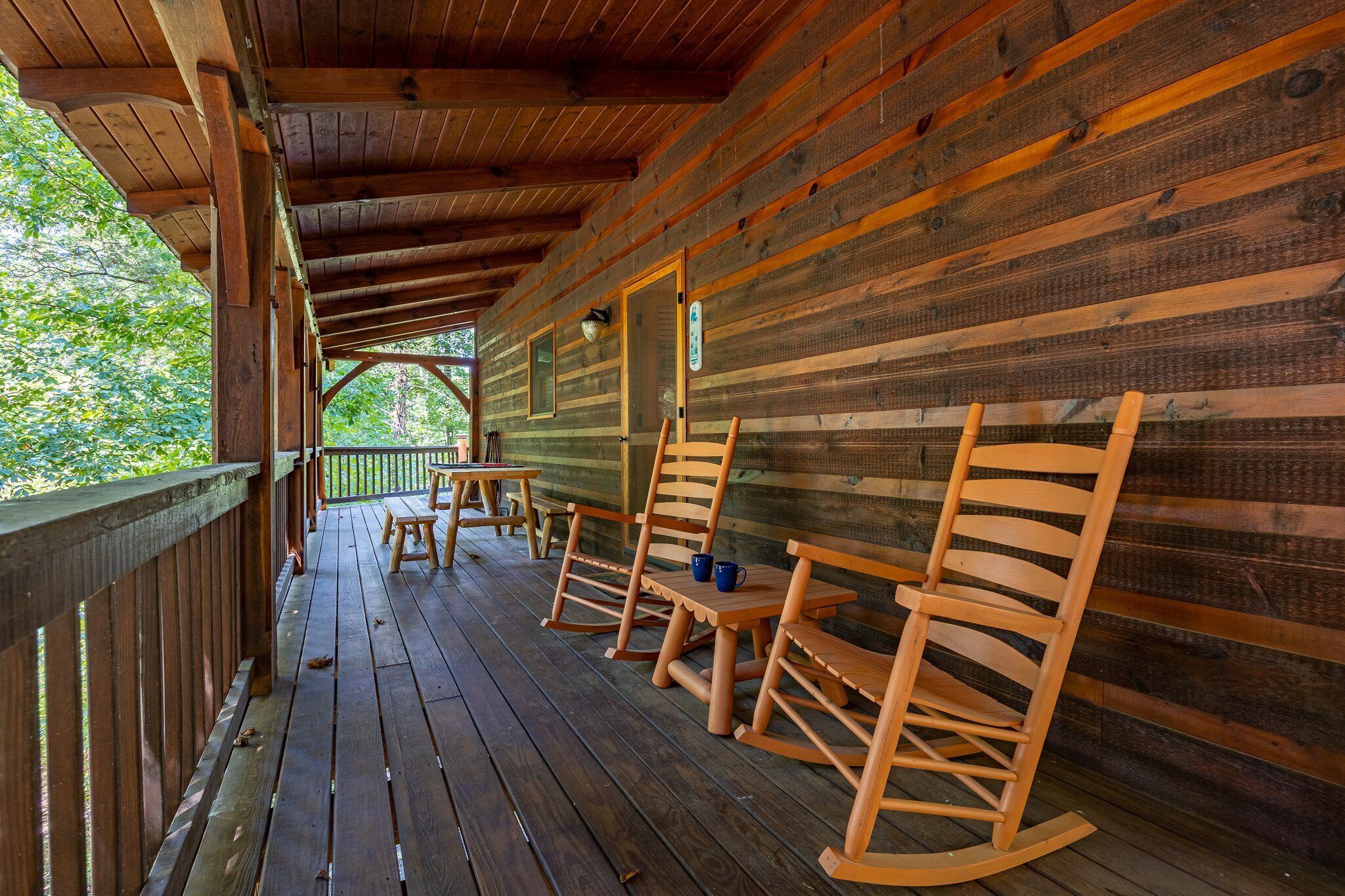 Una terraza de madera con mecedoras y mesas, rodeada de paredes y techo de madera.