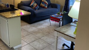 Un salon comprenant un canapé, une table basse, une lampe, ainsi qu’un coin cuisine avec un évier et un plan de travail.