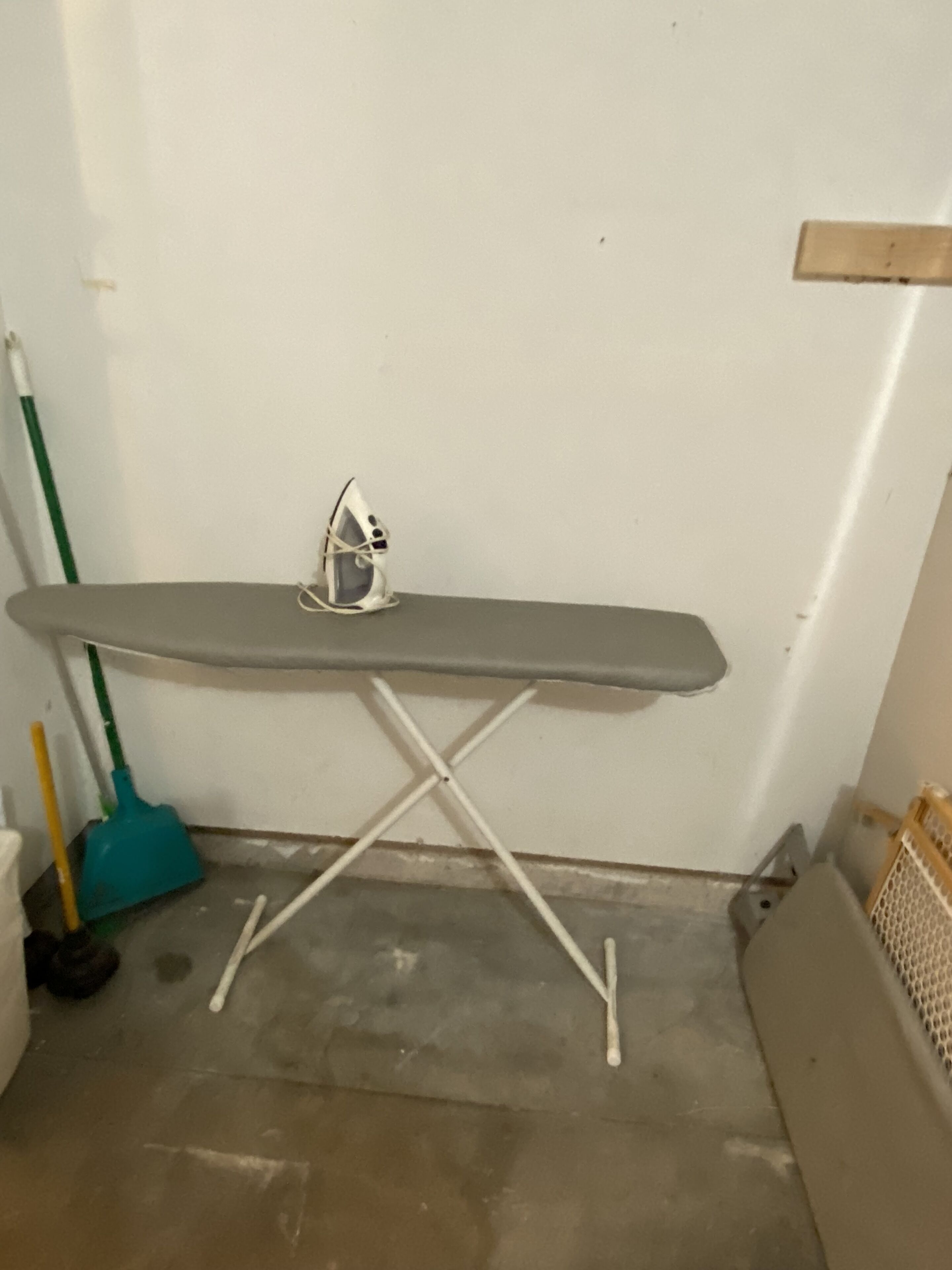 A small, portable ironing board with a white surface and a metal frame, placed on a concrete floor against a plain wall.