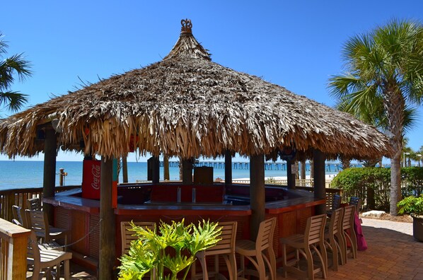 A beachside bar with a thatched roof, wooden chairs, and a view of the ocean.