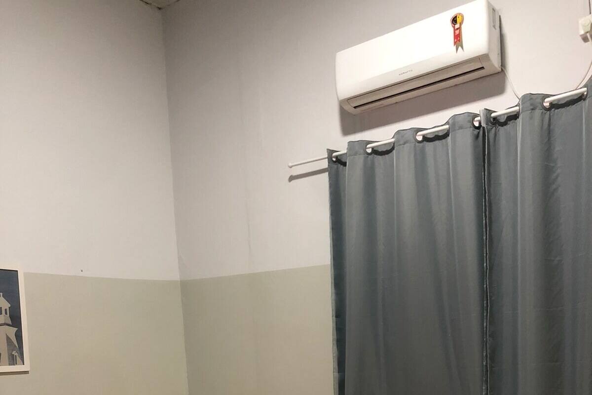 Ein Hotelzimmer mit drei Einzelbetten, jedes mit einer gesteppten Bettdecke und einem Kopfkissen. Eine Klimaanlage ist an der Wand oberhalb der Betten angebracht.