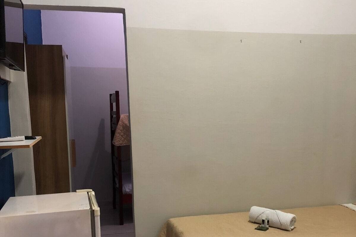 Ein kleines, schlichtes Zimmer mit einem Bett, einem kleinen Tisch und einem Kühlschrank.