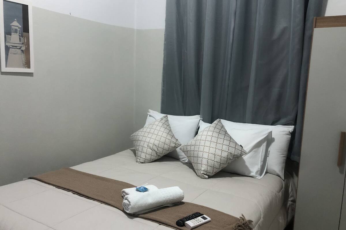 Ein ordentlich bezogenes Bett mit einer braunen Decke, weißen Kissen und einer Fernbedienung darauf.