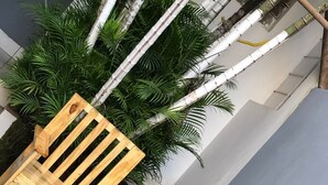 Two wooden chairs with slatted backs and armrests, placed on a dark floor with a white wall and green plants in the background. - Ágape Hotel (Rio Verde)