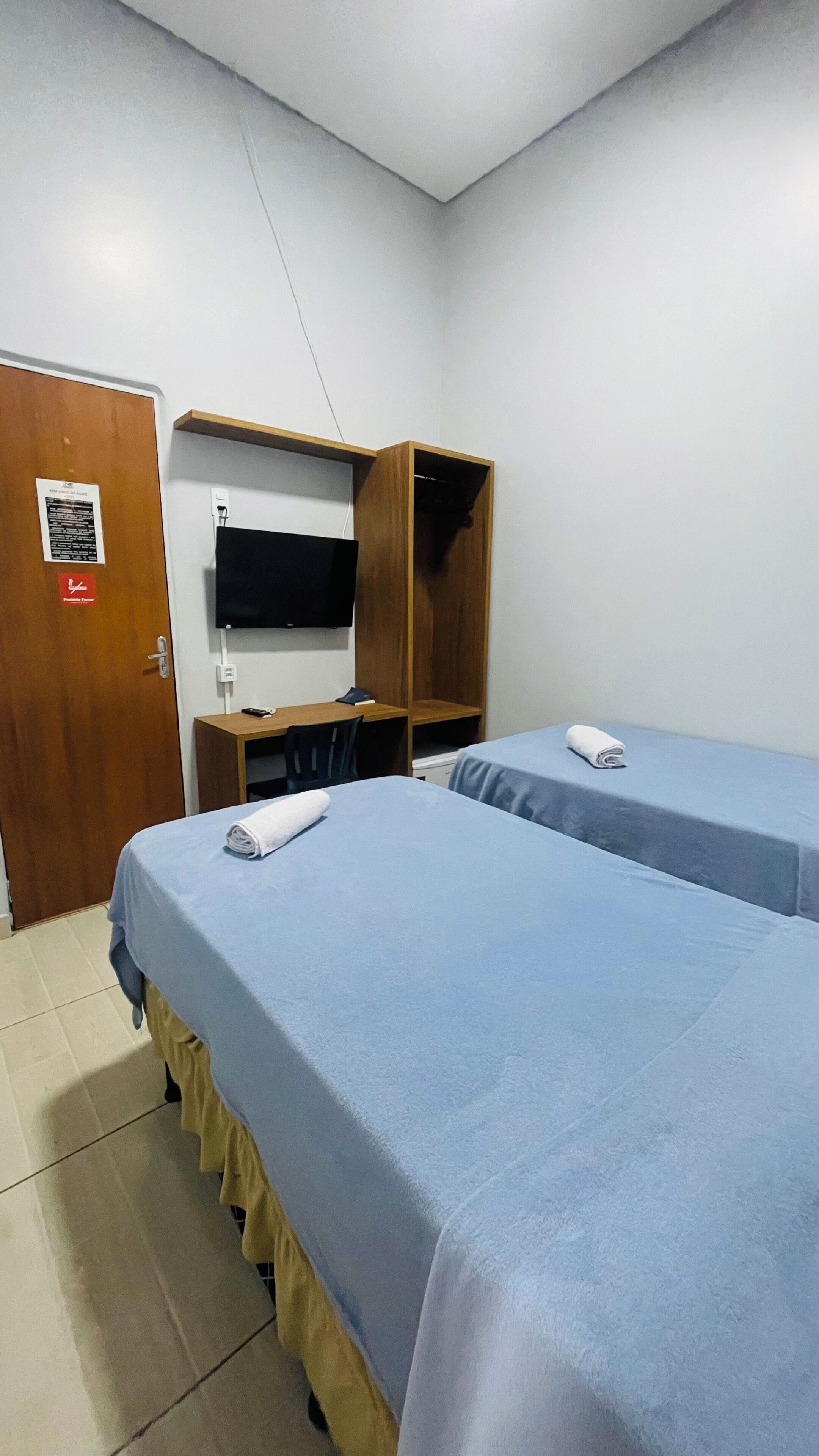 A hotel room with two beds, a wooden wardrobe, a desk, and a television.
