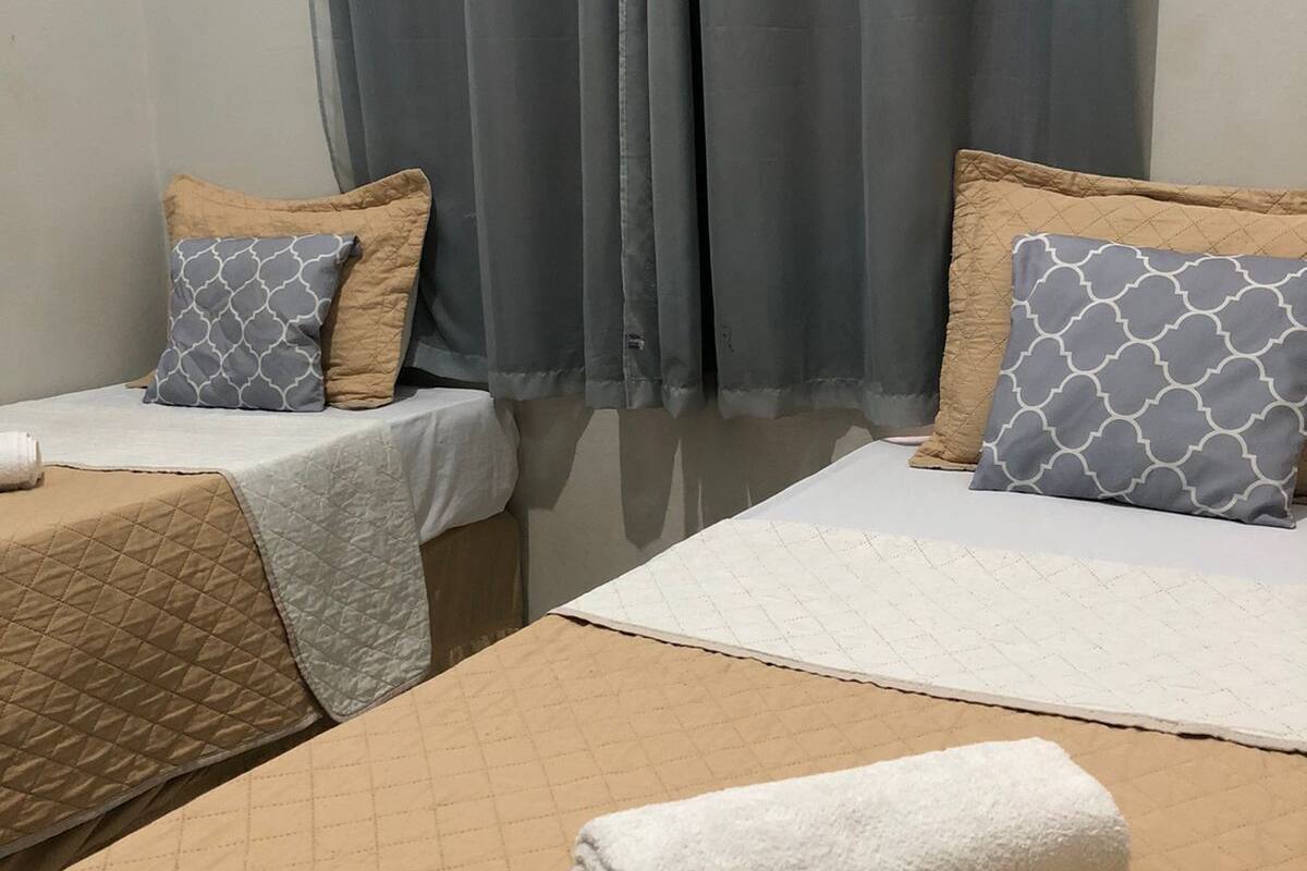Ein Hotelzimmer mit zwei Betten, jedes mit einer gemusterten Tagesdecke und passenden Kissen. Ein aufgerolltes weißes Handtuch liegt auf dem Boden.