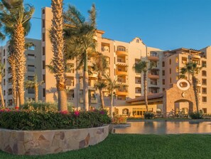A multi-story hotel with balconies, a swimming pool, and palm trees.