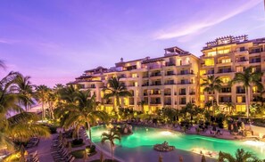 A hotel with a swimming pool surrounded by palm trees and lounge chairs.