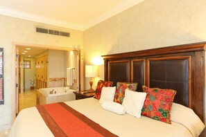 A hotel room with a large bed, a wooden headboard, a bathroom with a bathtub, and a mirror.