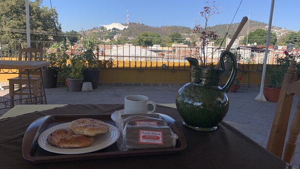 Una bandeja con pasteles y una taza en una mesa, con vista a un paisaje urbano y una colina al fondo.