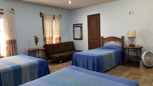Habitación de hotel con dos camas, un sofá, una mesa, un espejo y un ventilador.