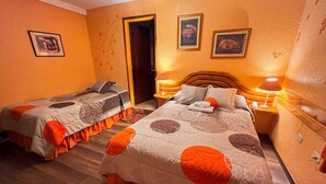 Una habitación con dos camas, cada una con una colcha y almohadas estampadas. Hay dos mesitas de noche con lámparas, una puerta y decoración en la pared.