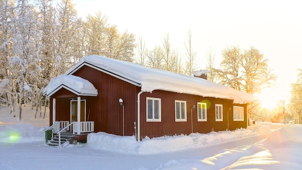 Een houten blokhut met een veranda en wenteltrap, omringd door met sneeuw bedekte bomen.